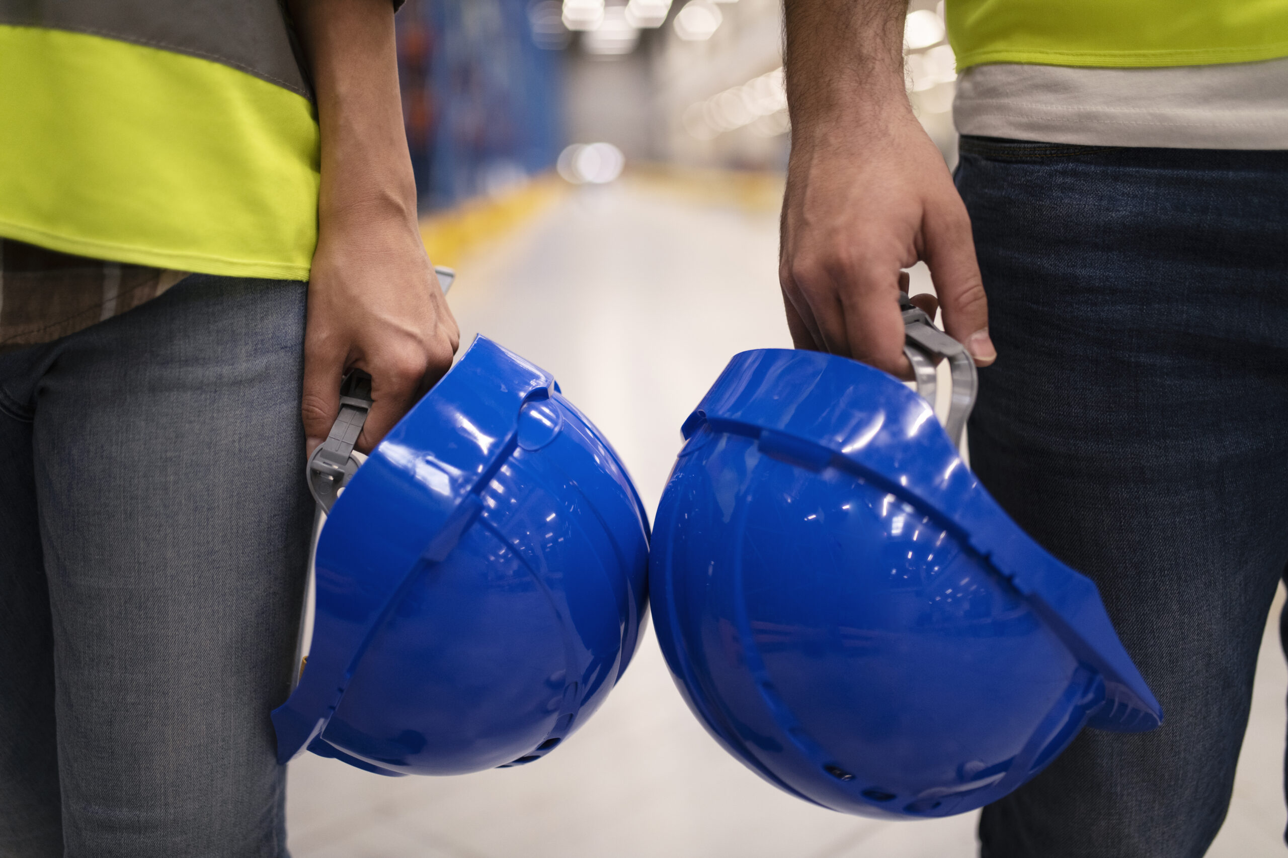 Close up of two unrecognizable industrial workers holding hardhat protection helmets.